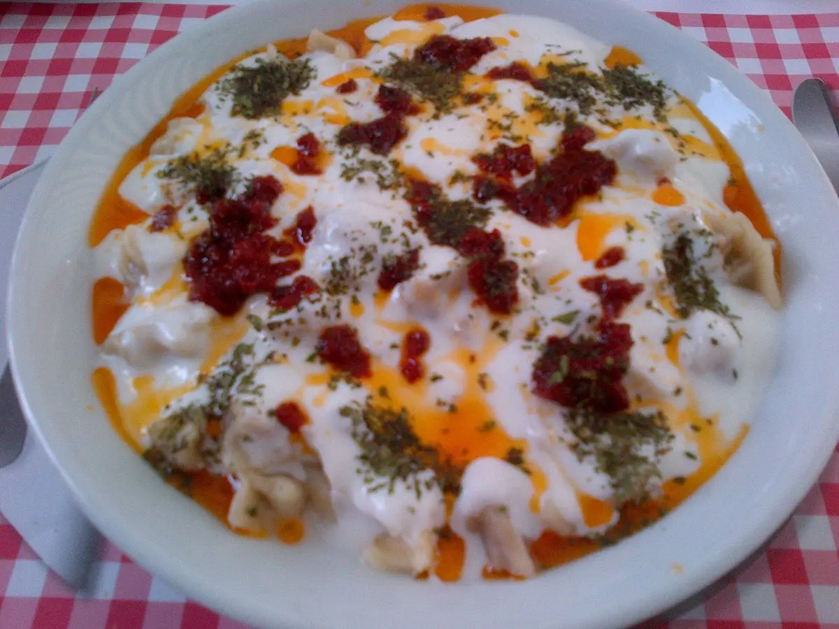 Plato de pasta rellena turca con yogur, pimentón rojo y hierbas sobre mantel de cuadros