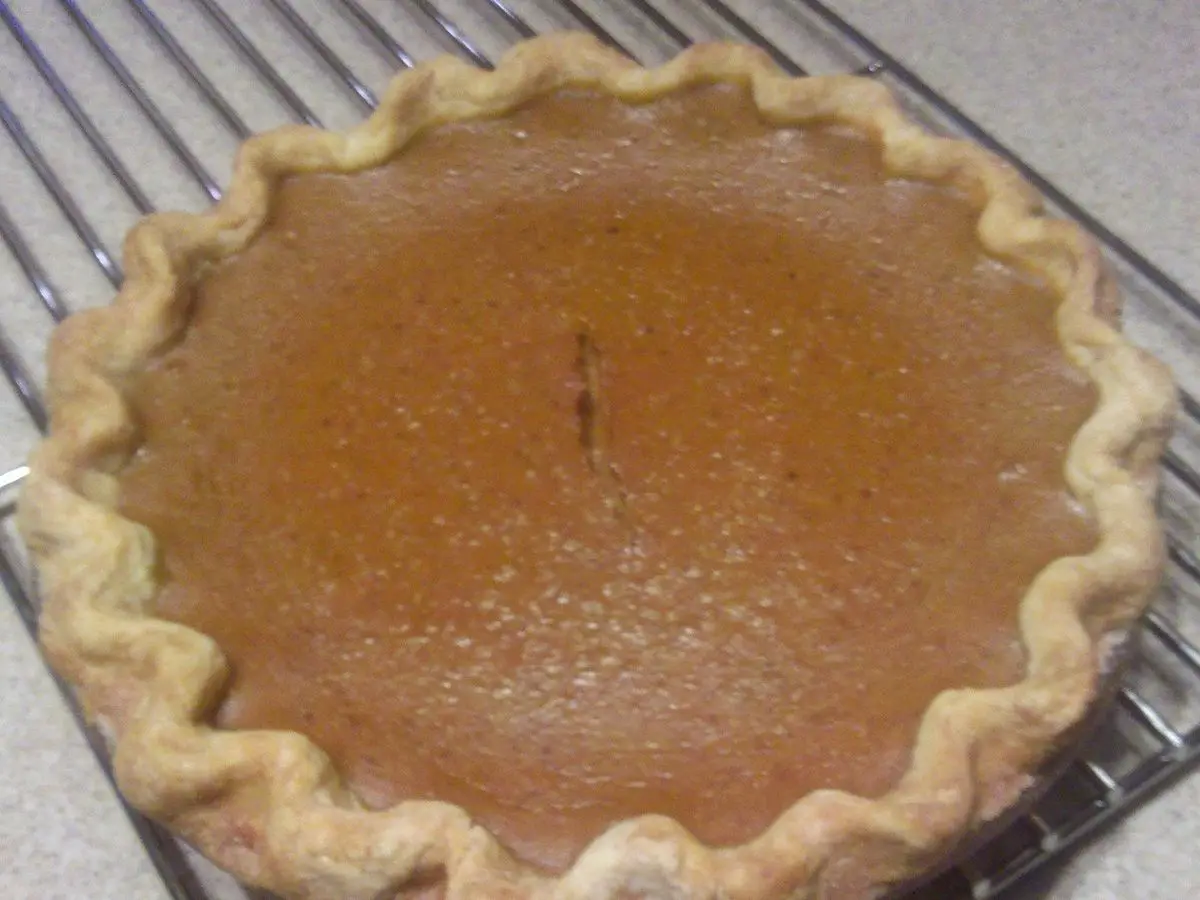 Pastel de calabaza de color naranja con borde de masa ondulado sobre una rejilla