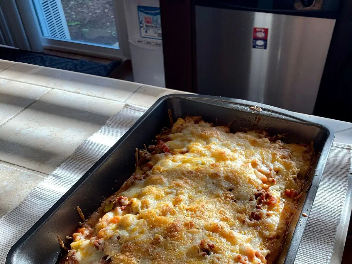 Fuente metálica con pastel gratinado de queso fundido dorado sobre una encimera