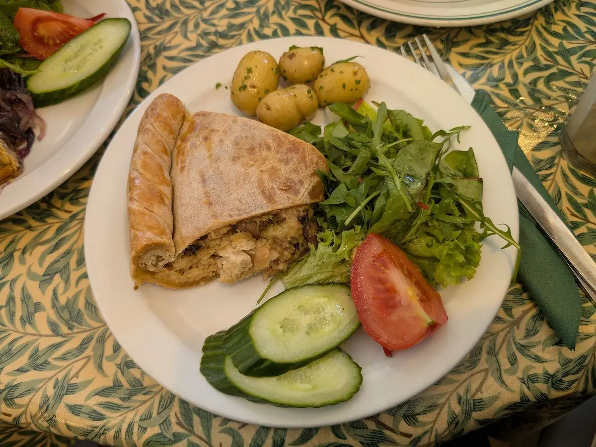 Porción de pastel de pollo y puerro con hojaldre, patatas nuevas, rúcula, tomate y pepino en un plato