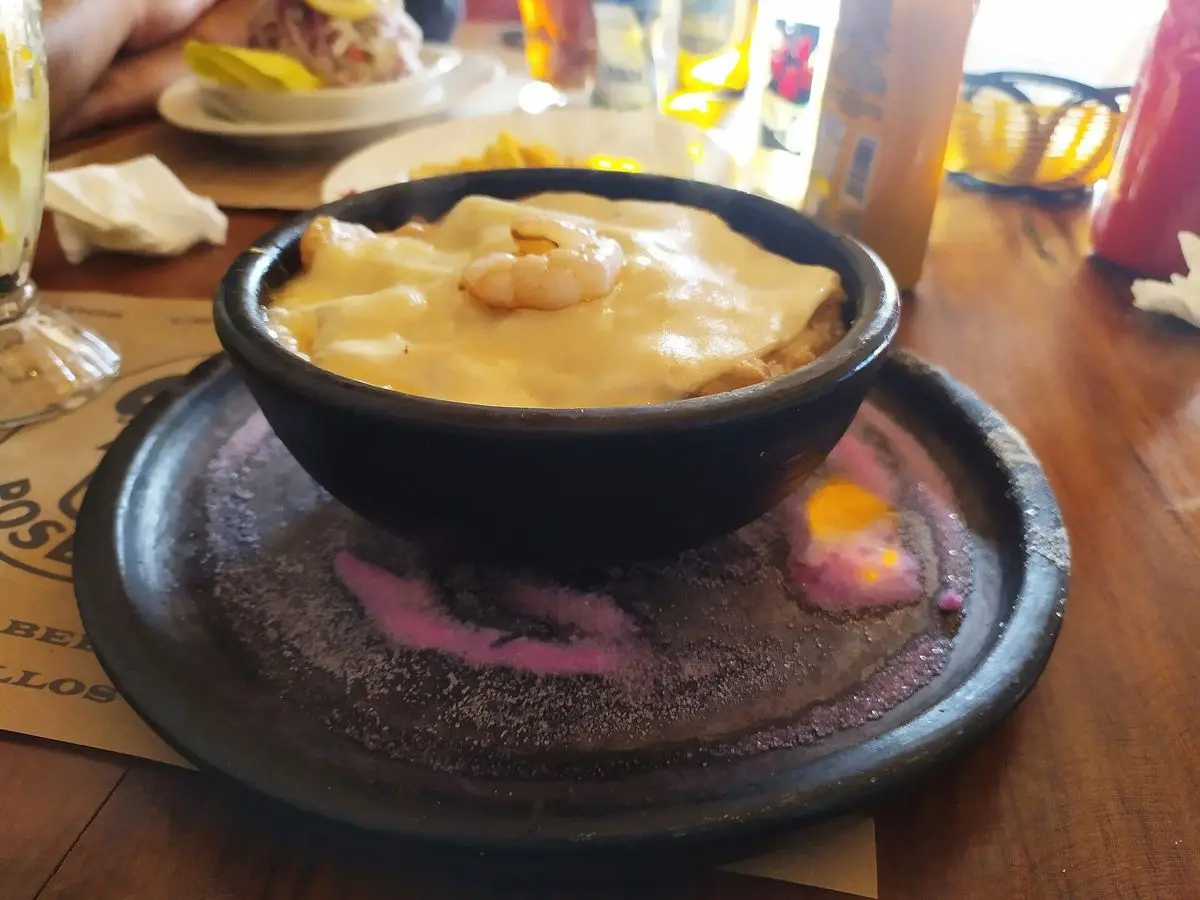 Cazuela negra de pastel de jaiba gratinado servida sobre un plato de piedra en una mesa de madera