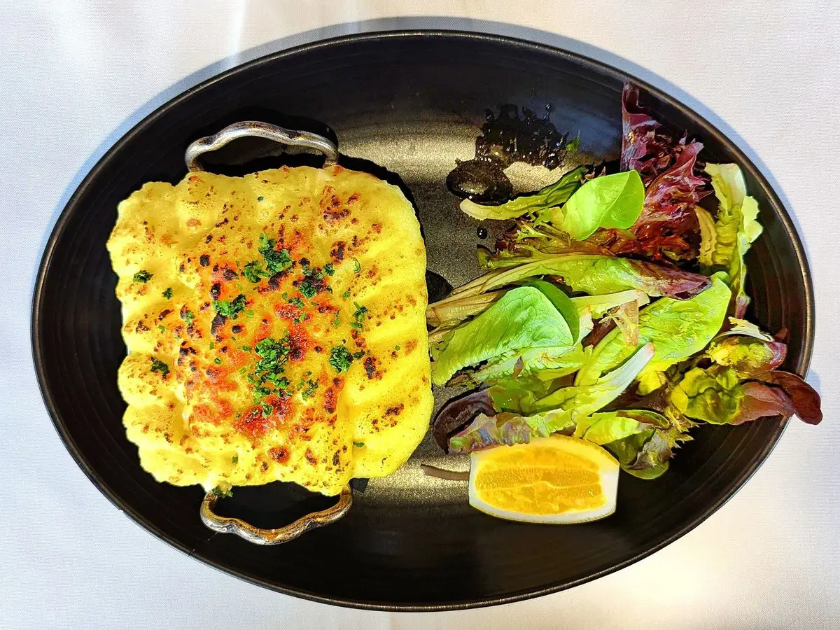 Pastel de pescado dorado y gratinado en fuente negra con ensalada de hojas y medio huevo cocido