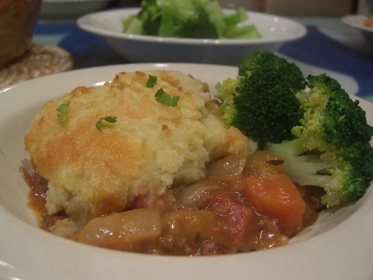 Ración de pastel de carne con puré de patata gratinado y brócoli en un plato blanco
