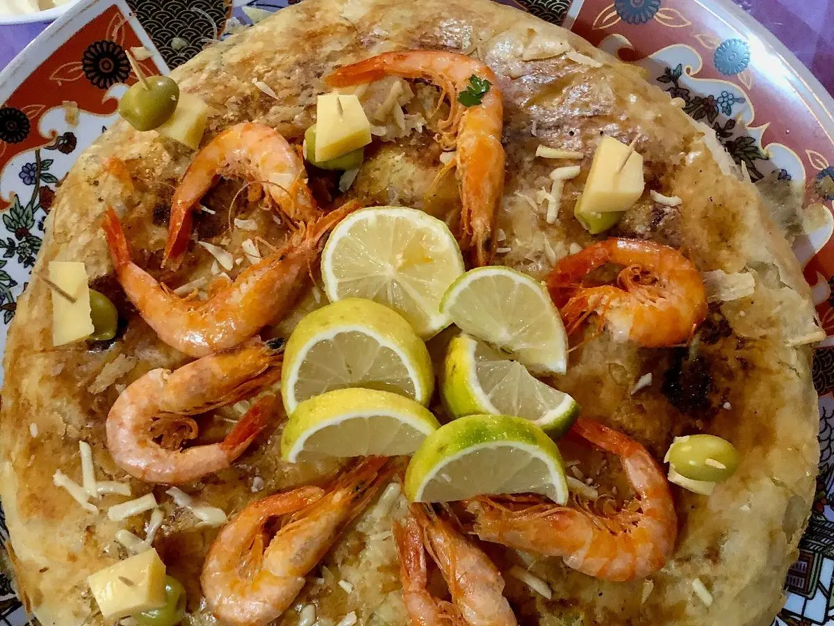 Pastela redonda de marisco cubierta con gambas enteras y rodajas de lima sobre fideos finos