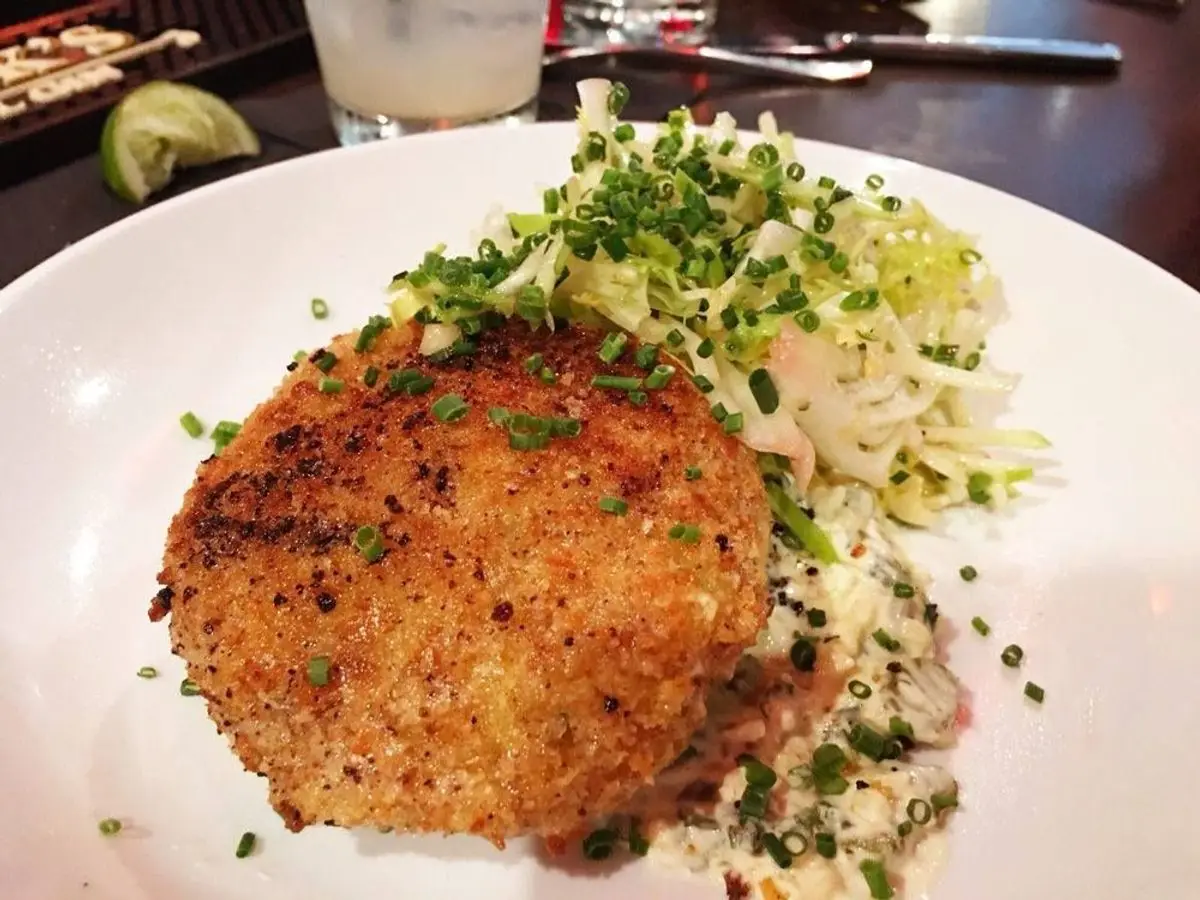 Pastelito de cangrejo dorado con ensalada fresca y cebollino picado en un plato blanco