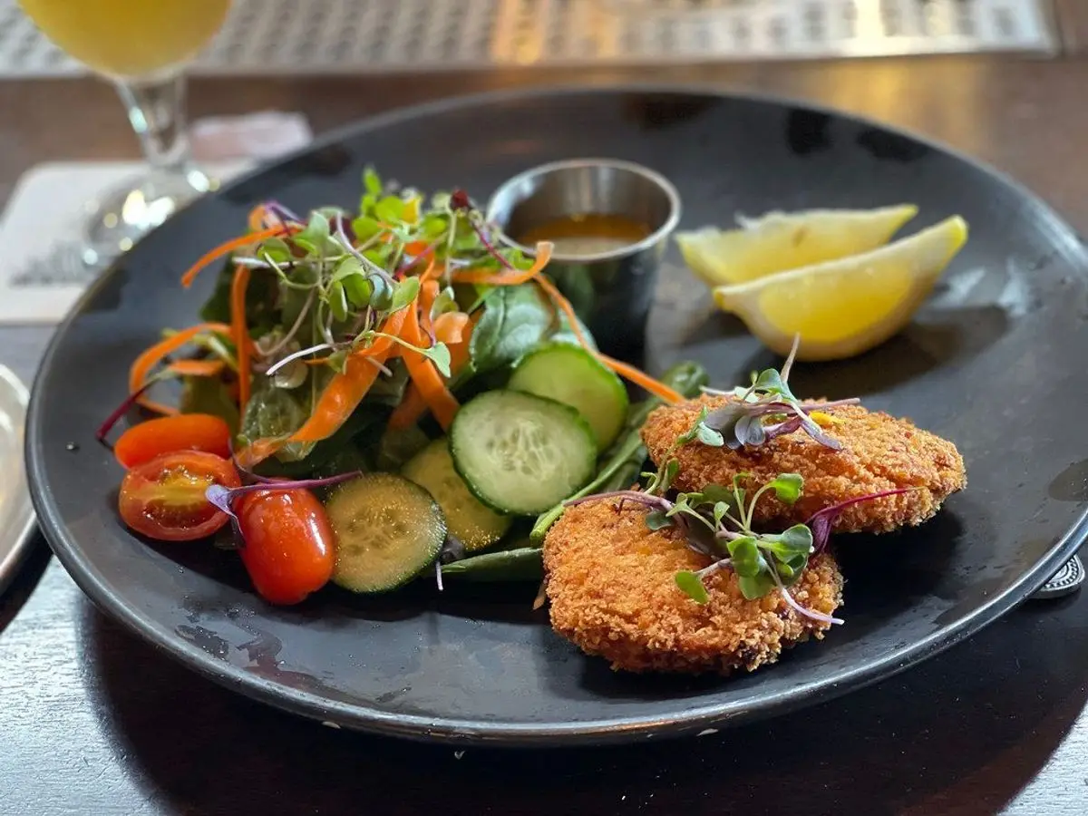 Dos tortitas de pescado empanadas con ensalada de lechuga, tomate y pepino en un plato oscuro