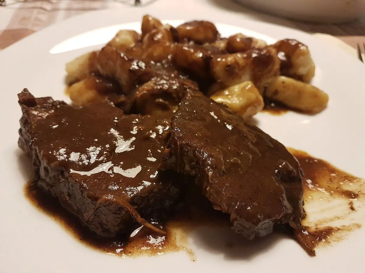 Asado de ternera en salsa oscura brillante con ñoquis dorados en un plato blanco
