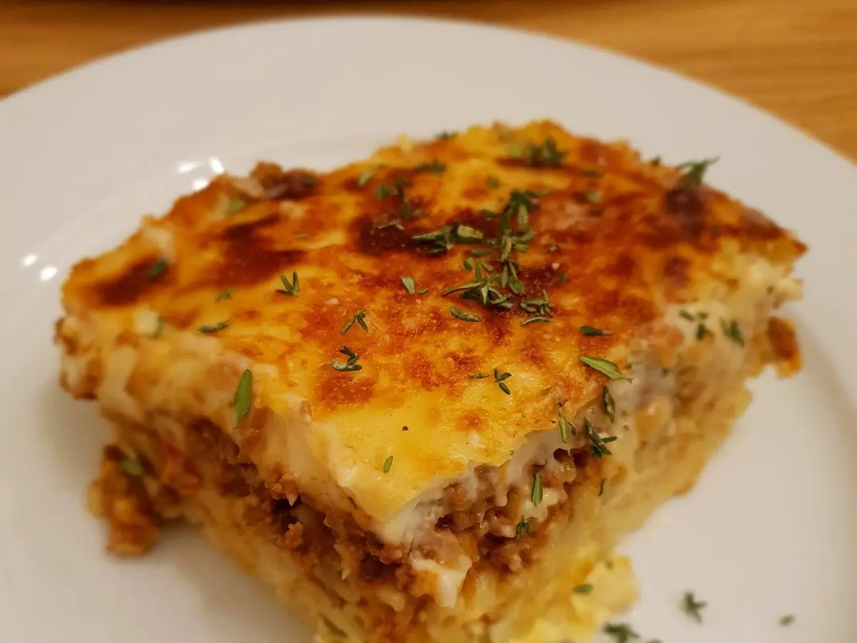 Porción de pastitsio gratinado con macarrones, carne picada y tomillo en un plato blanco