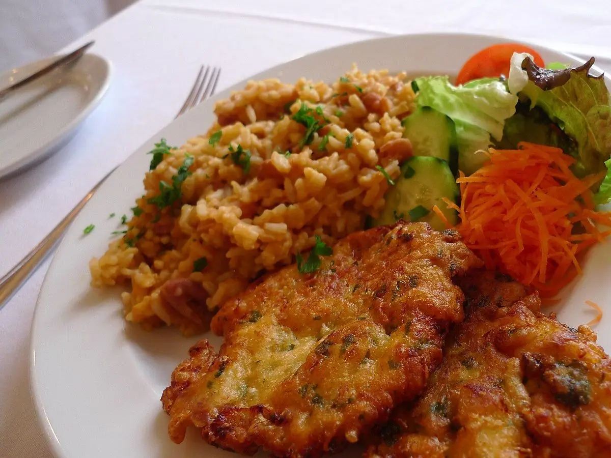 Pataniscas de bacalao doradas con arroz de tomate, zanahoria rallada y lechuga en un plato blanco
