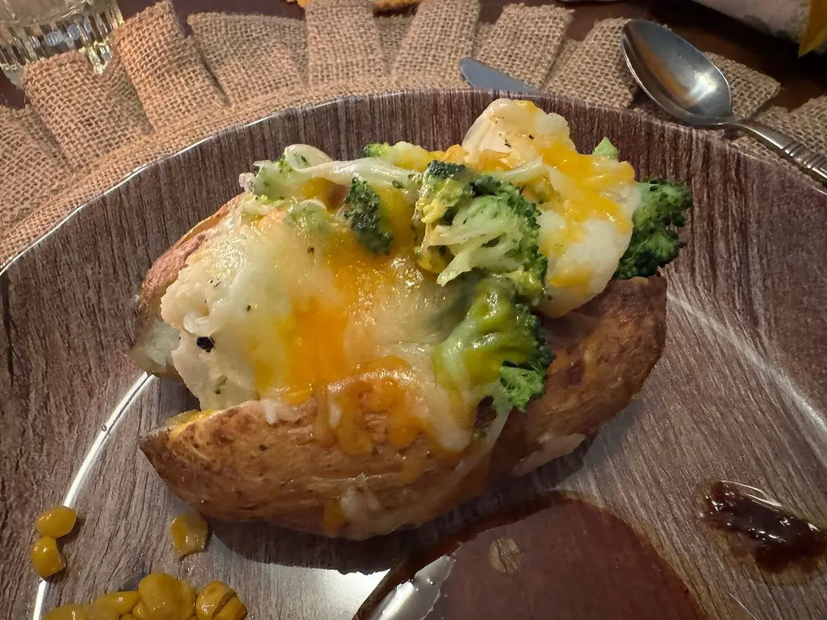Patata asada abierta y rellena de brócoli y queso gratinado con huevo, servida en un plato marrón