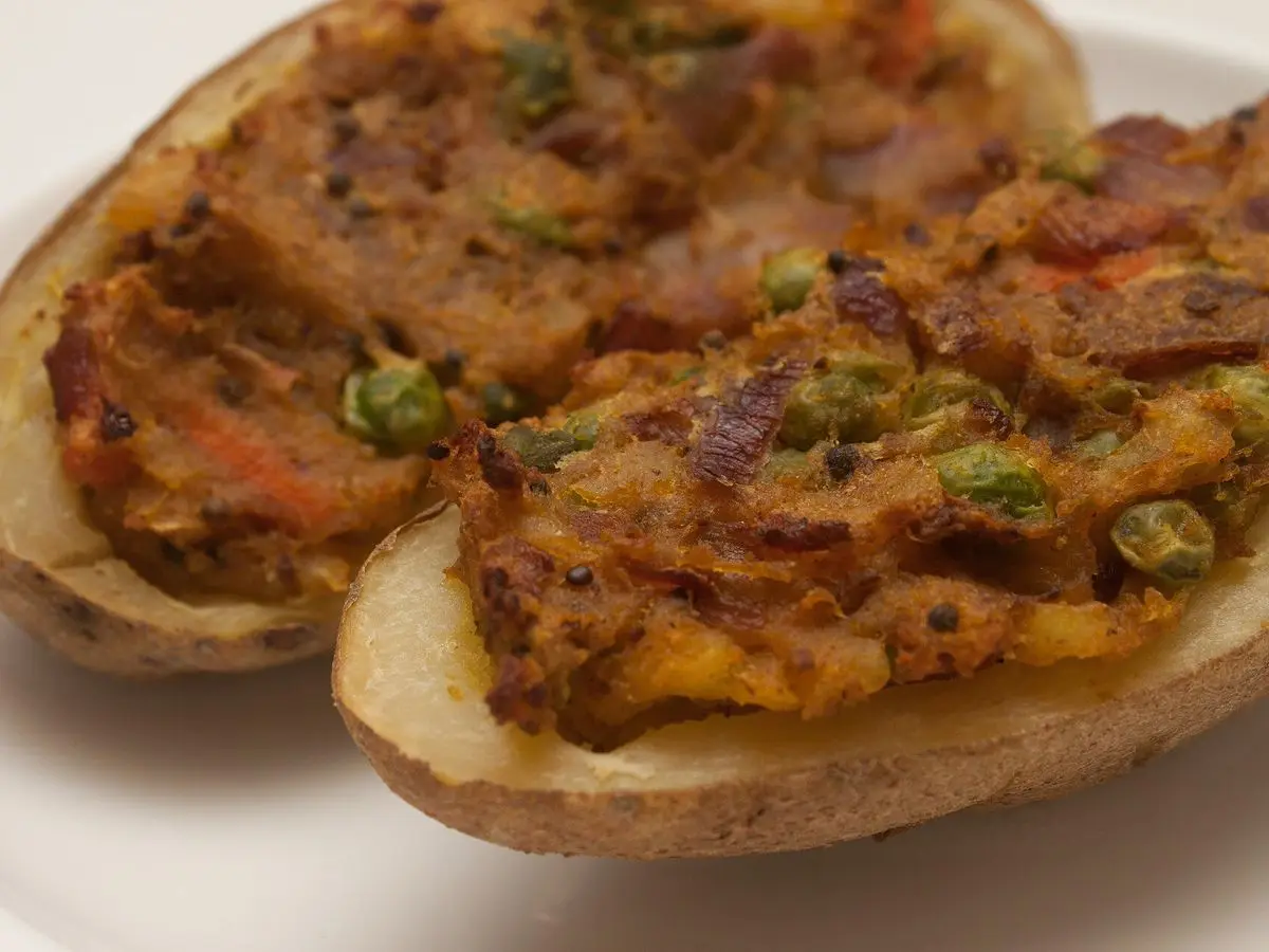 Dos mitades de patata asada rellenas de verduras y cebollino sobre un fondo blanco