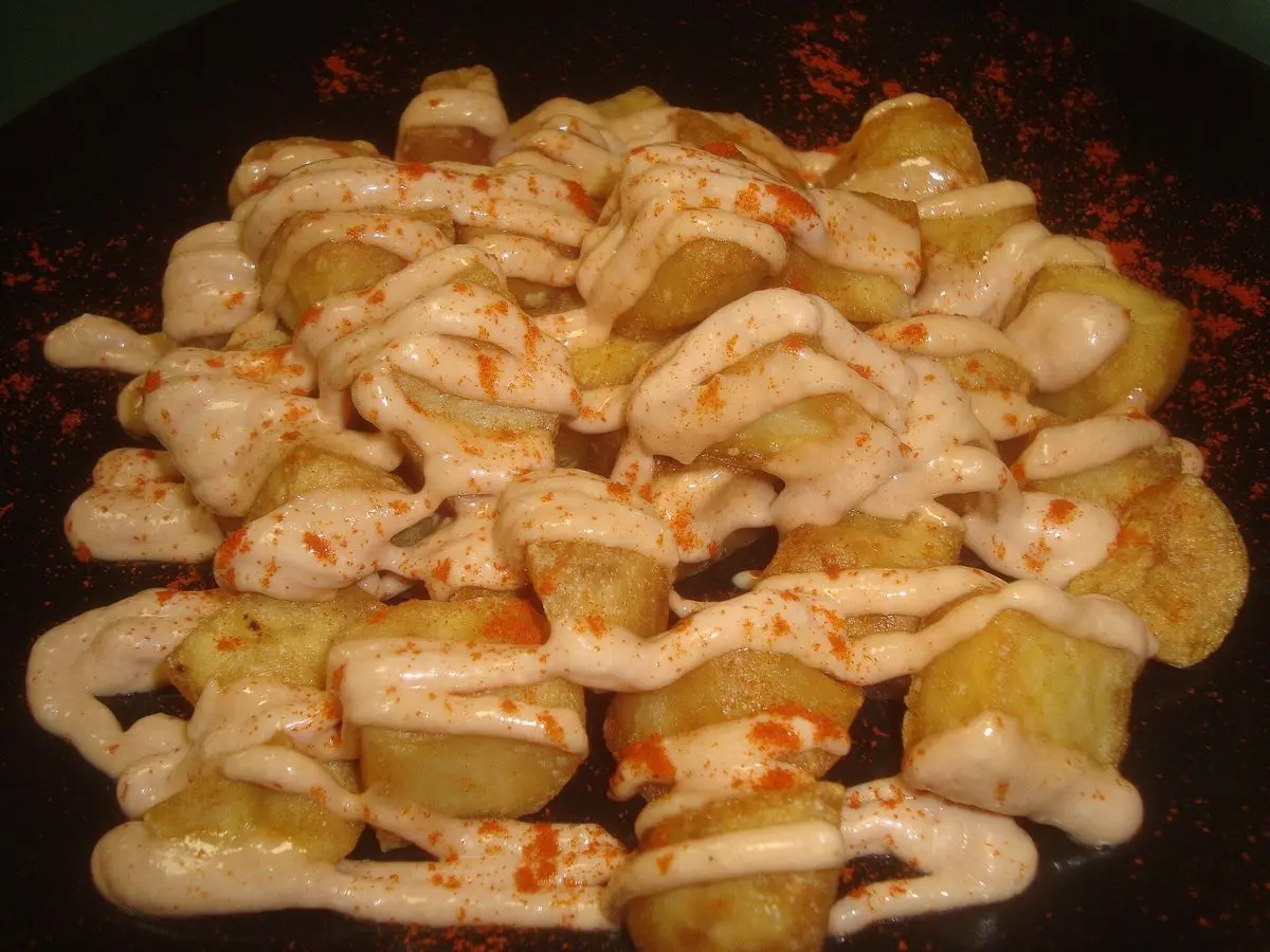 Patatas en dados doradas con salsa rosada y pimentón sobre una bandeja negra