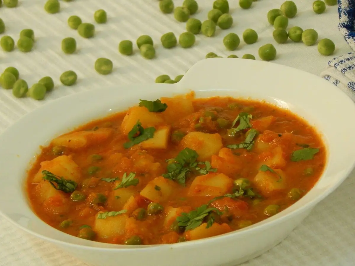 Cuenco blanco de patatas guisadas con guisantes en salsa de tomate con hierbas, con guisantes sueltos alrededor