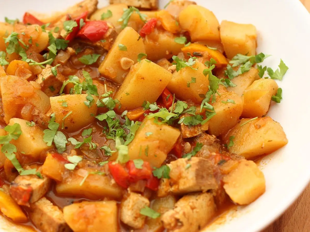 Guiso de patata con pimiento rojo, pimentón y perejil picado en un plato blanco