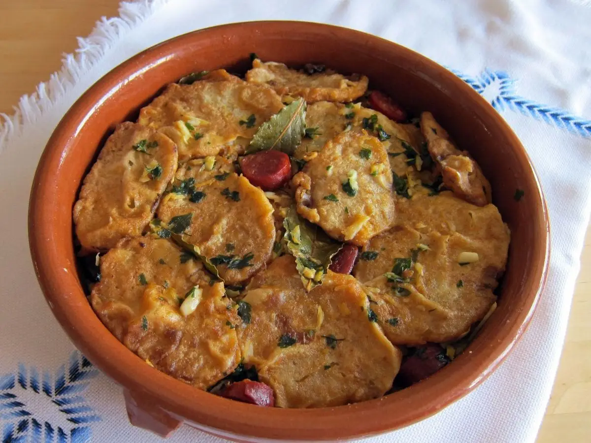 Cazuela de barro con rodajas de patata rebozadas y perejil sobre un mantel blanco