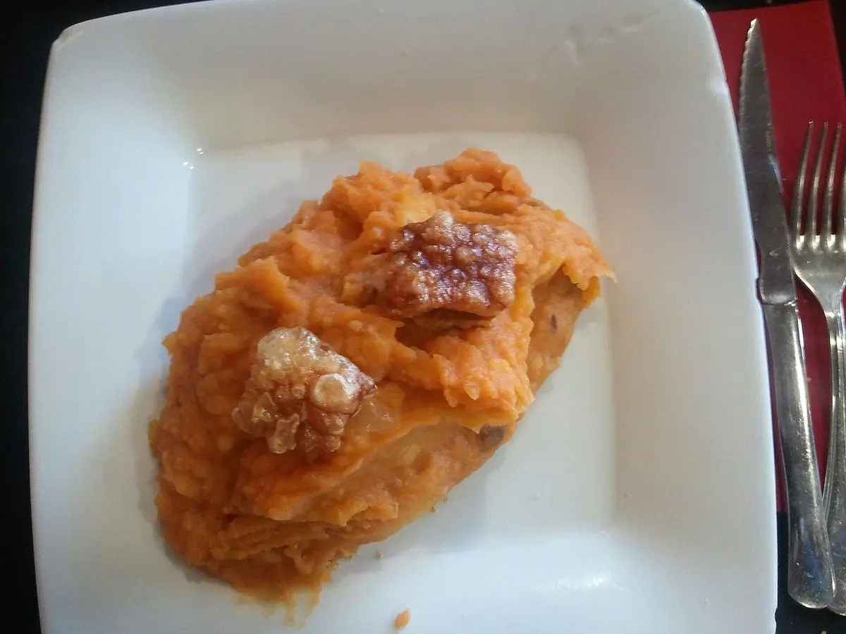Plato blanco con puré de patata anaranjado y torreznos