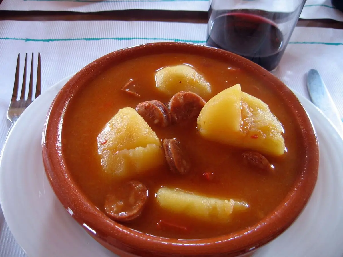 Cazuela de barro con patatas guisadas en salsa roja y rodajas de chorizo