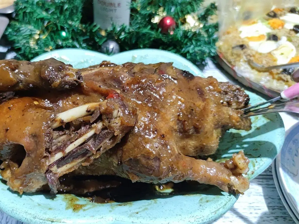 Pato entero guisado y brillante, de color caoba, servido en una fuente azulada