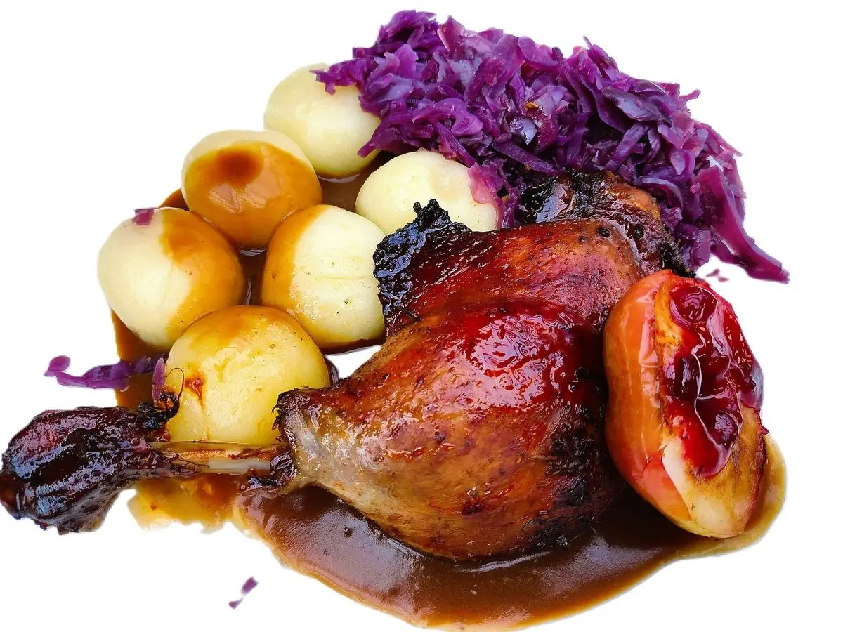 Muslo de pato asado y brillante con lombarda, patatas pequeñas y media manzana asada