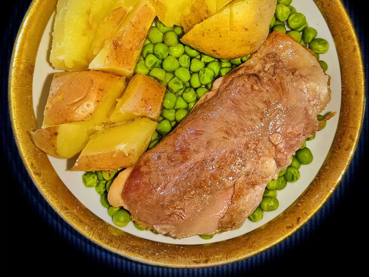 Filete de pato asado con patatas cocidas y guisantes en un plato con borde dorado