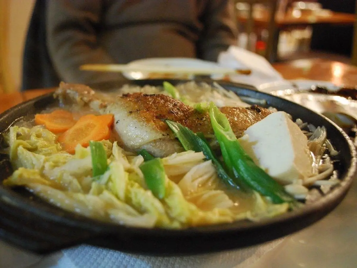 Cazuela negra de pato con col china, cebolleta y zanahoria en caldo