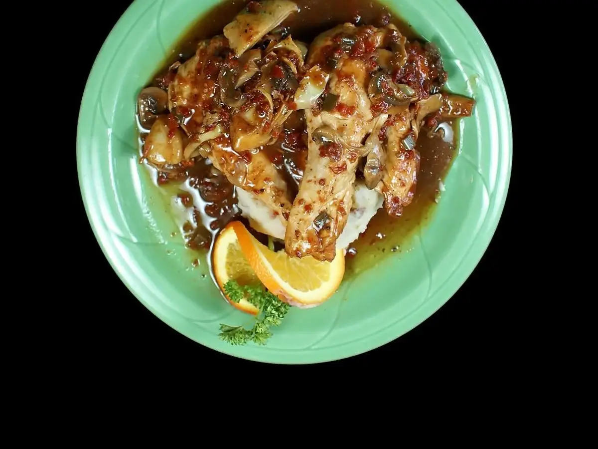 Pechuga de pato laminada en salsa oscura con rodaja de naranja sobre un plato verde