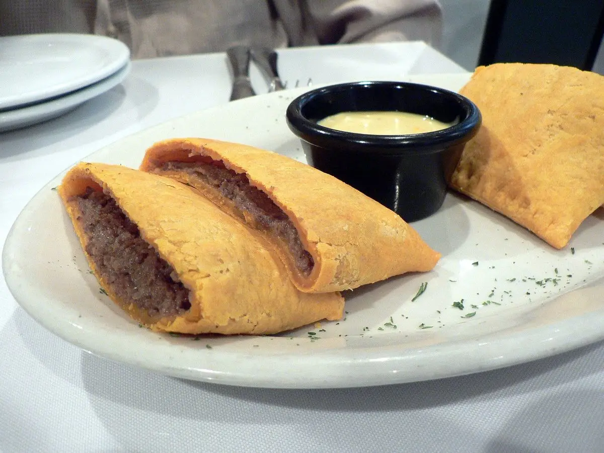 Patties jamaicanos de masa amarilla abiertos con relleno de carne en un plato blanco