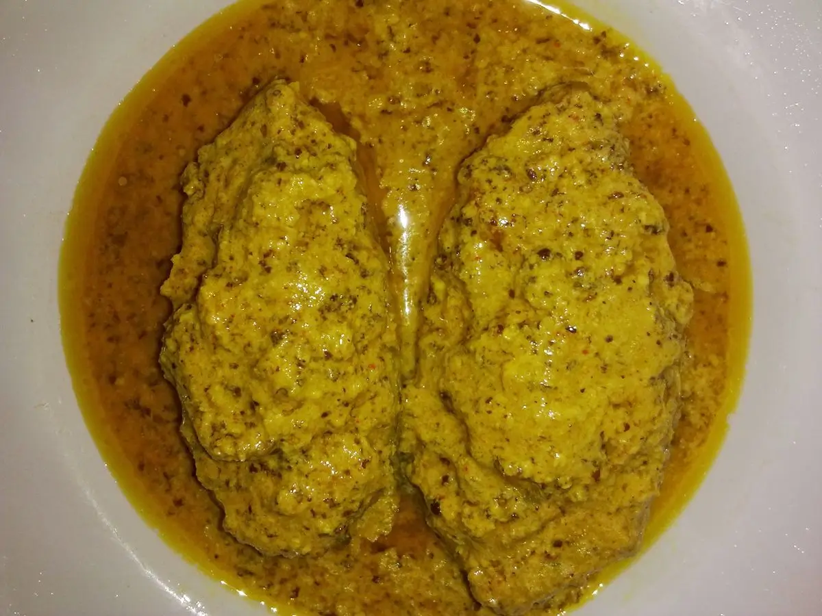 Dos piezas de pescado cubiertas de pasta de mostaza en una salsa amarilla dentro de un plato blanco