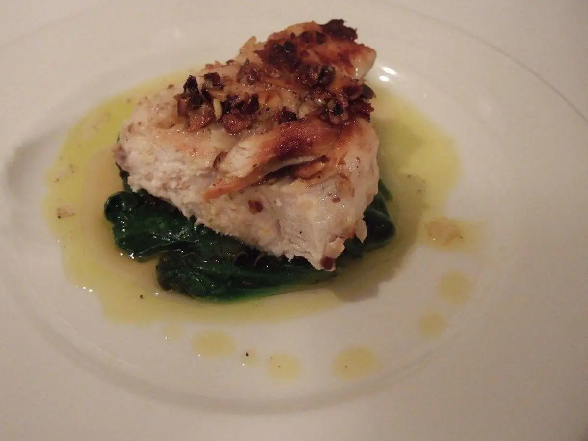 Pechuga con costra de almendra sobre cama de espinacas y aceite de oliva en un plato blanco