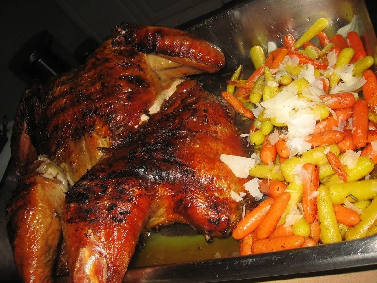 Pavo asado dorado en una bandeja junto a pimientos, cebolla y zanahoria troceados