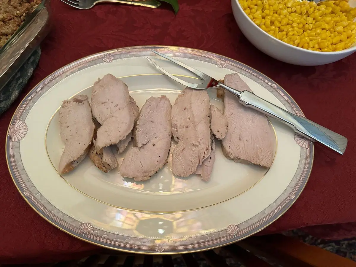 Pechuga de pavo cocinada cortada en lonchas sobre un plato decorado, con un cuenco de maíz al fondo