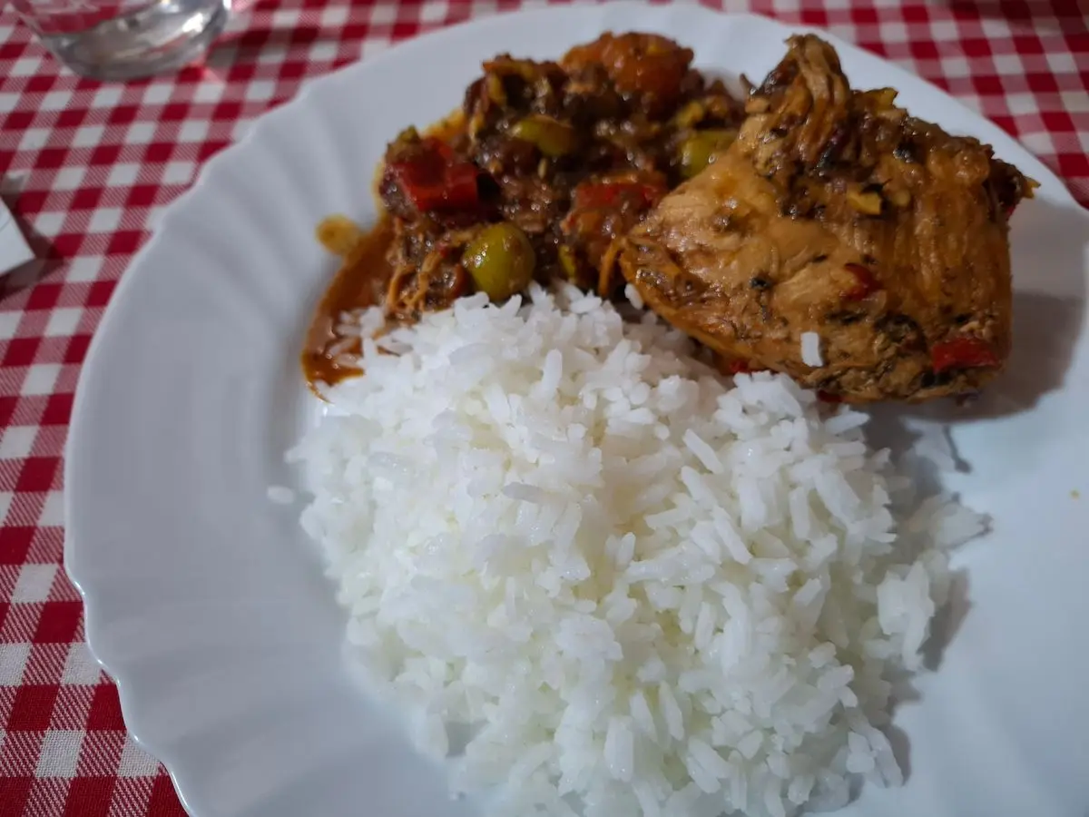 Pavo guisado en salsa con pimiento y aceitunas junto a arroz blanco, sobre un mantel de cuadros