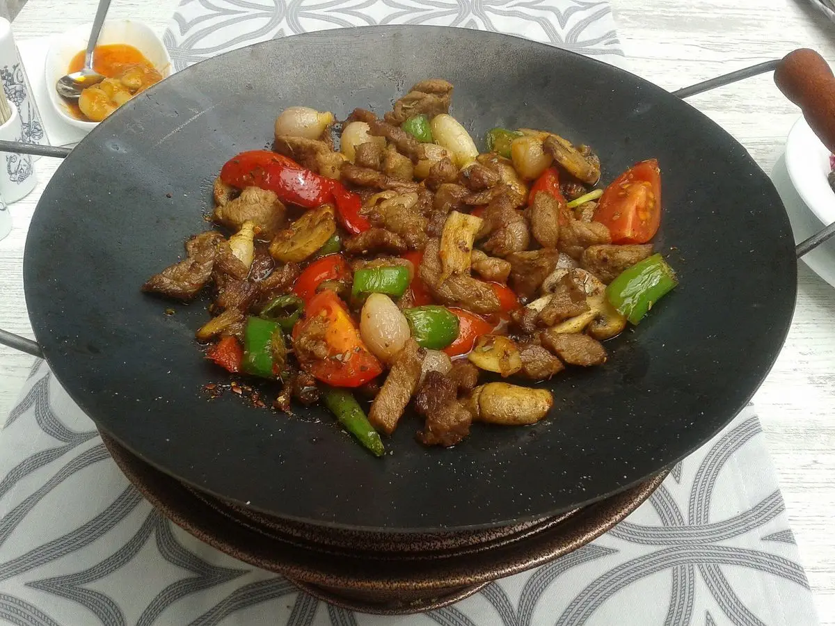Sartén negra con carne salteada, pimiento rojo y verde y frutos secos