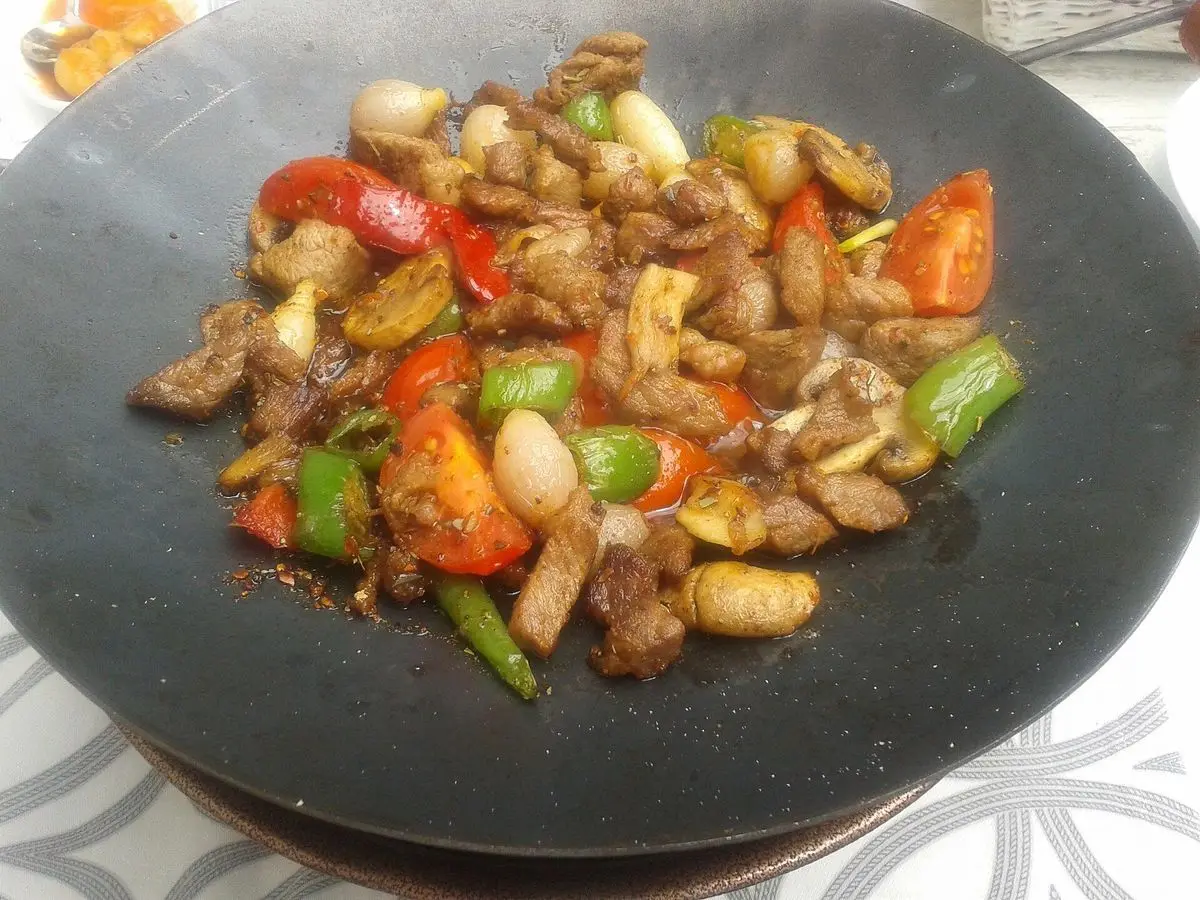Salteado de carne en trocitos con pimiento rojo y verde y frutos secos en una sartén negra