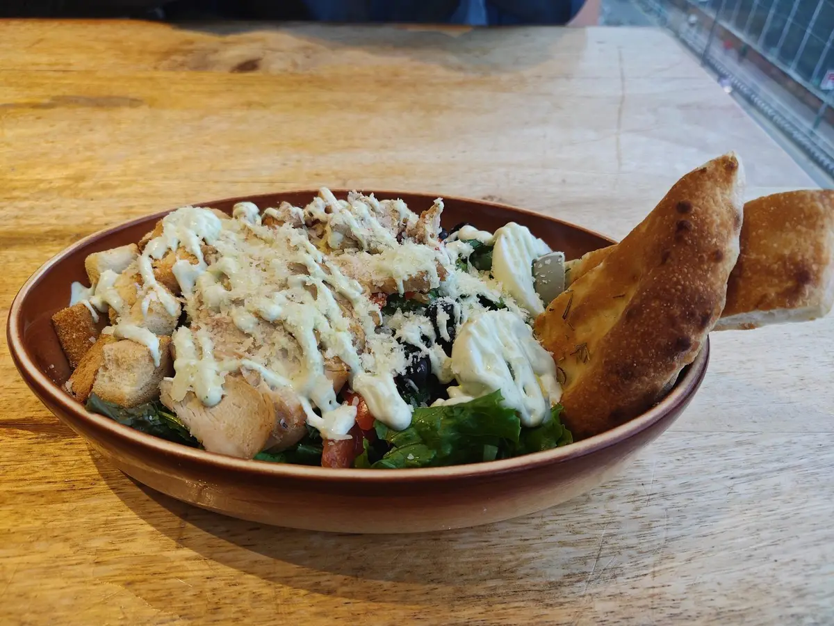 Bol de ensalada con pollo en dados, hojas verdes y salsa blanca