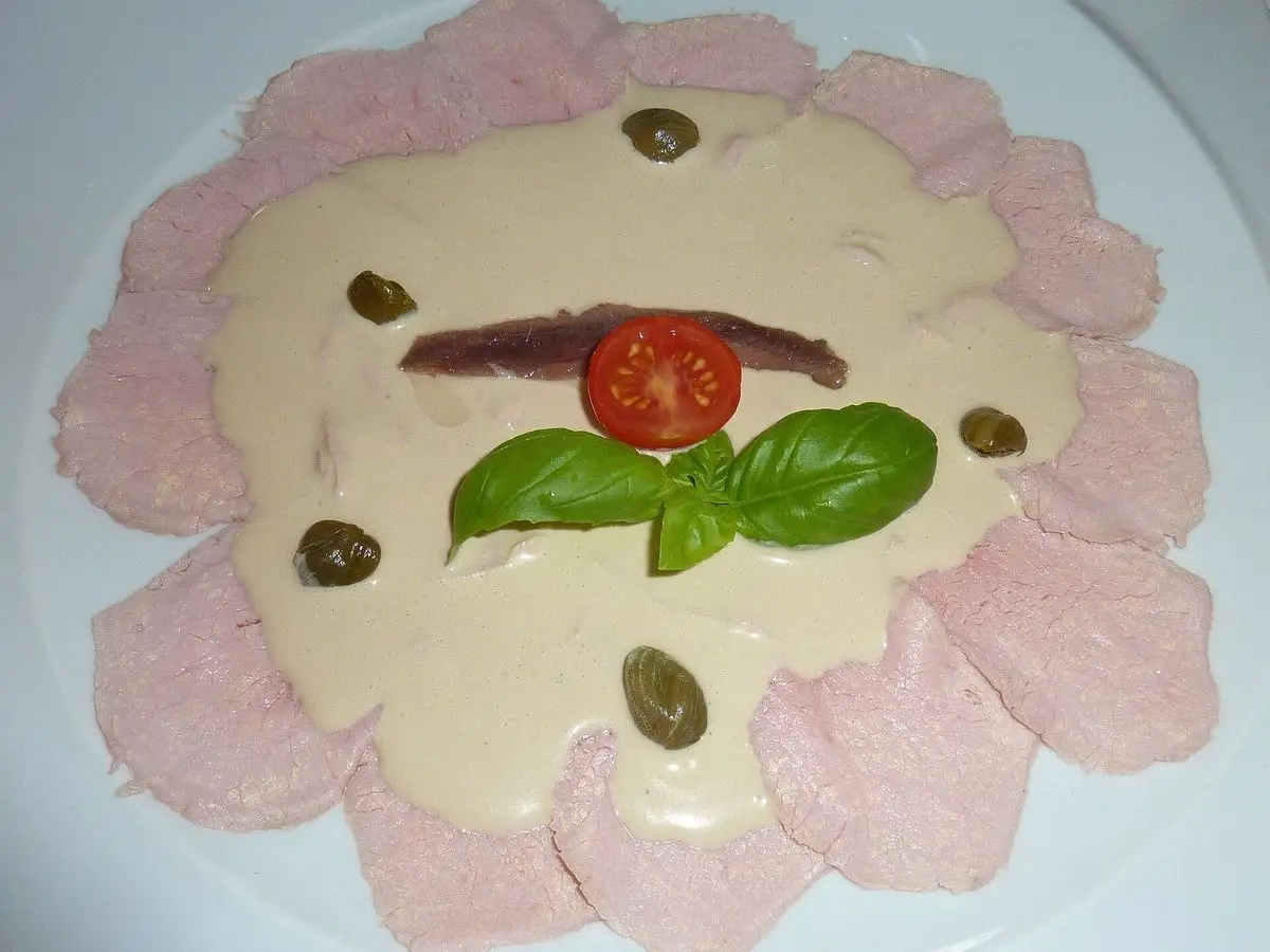 Lonchas de carne fría con salsa cremosa de atún, alcaparras, tomate y albahaca en un plato