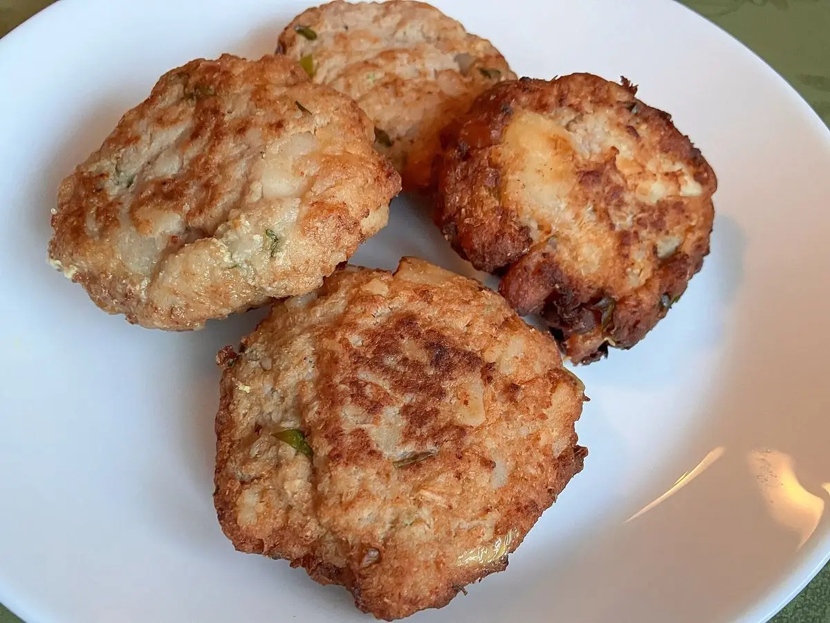 Tres tortitas doradas de carne y yuca fritas servidas en un plato blanco
