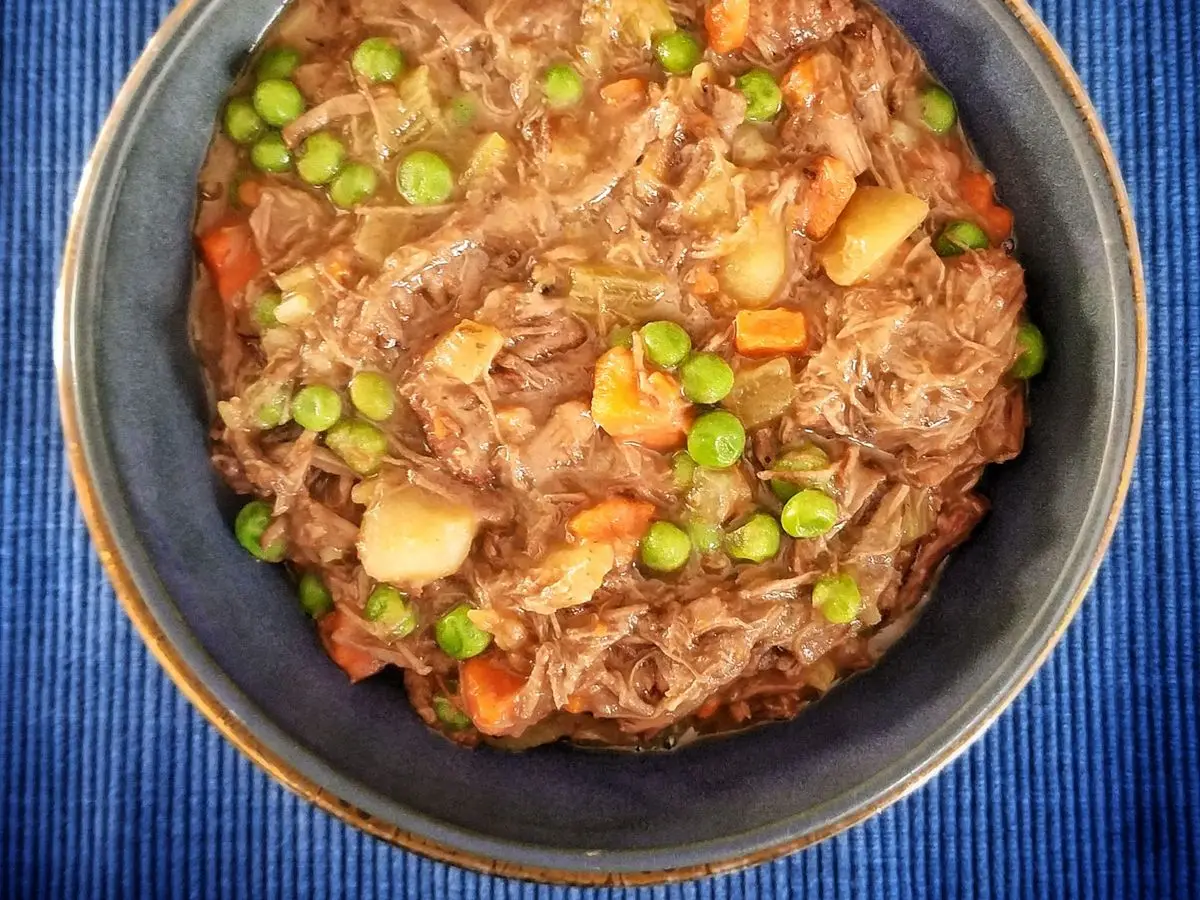 Cuenco azul con ternera desmenuzada guisada con guisantes, zanahoria y patata