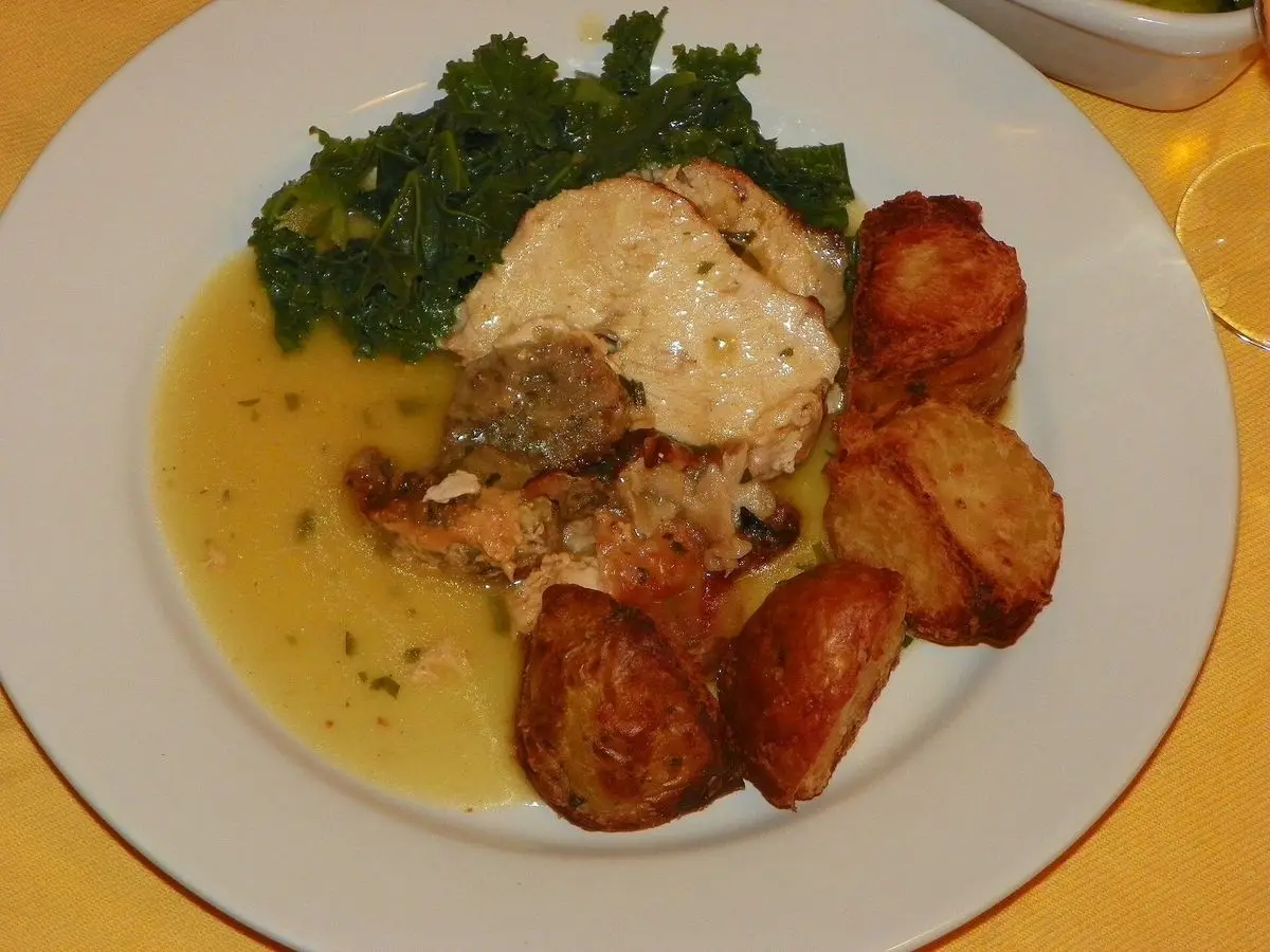 Pavo asado relleno con salsa, patatas asadas y col rizada en un plato blanco