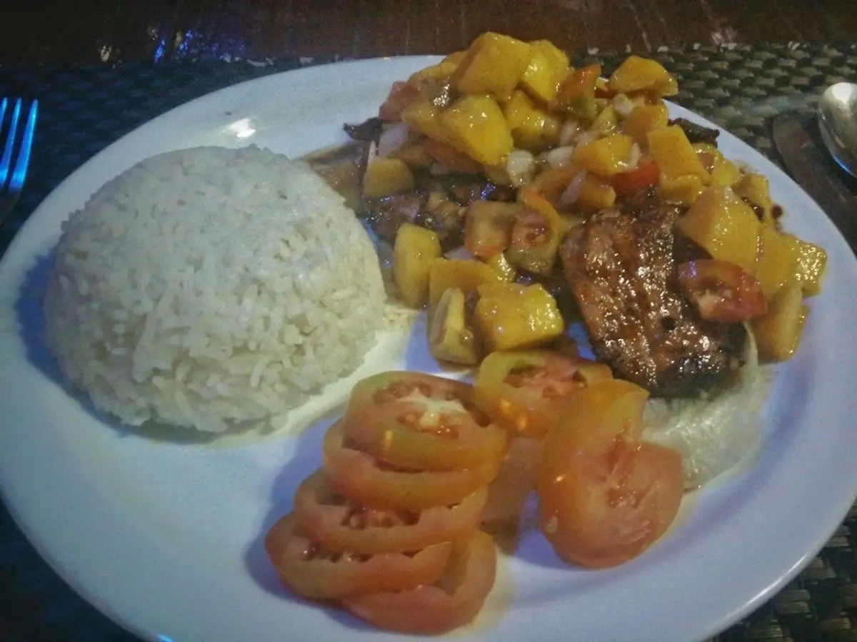 Plato con arroz blanco, carne con dados de mango y piña, y rodajas de tomate