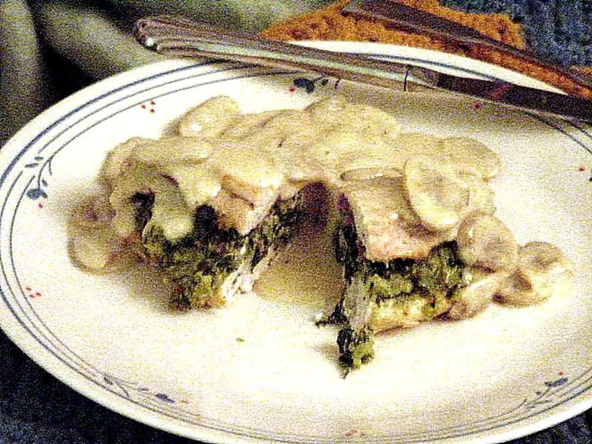 Pechuga de pollo rellena de espinacas abierta y cubierta con salsa cremosa de champiñones en un plato
