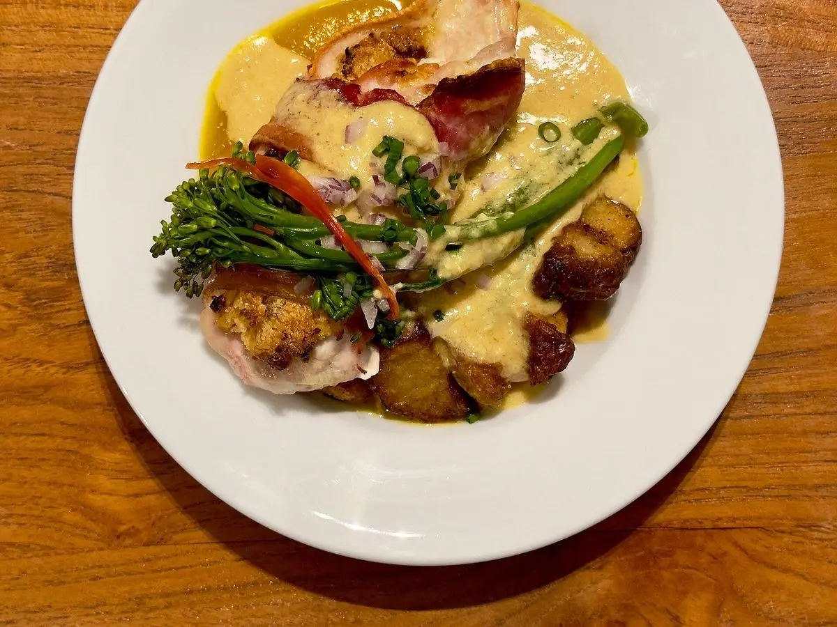 Pechuga de pollo rellena con salsa, espárragos verdes y patatas doradas en un plato blanco