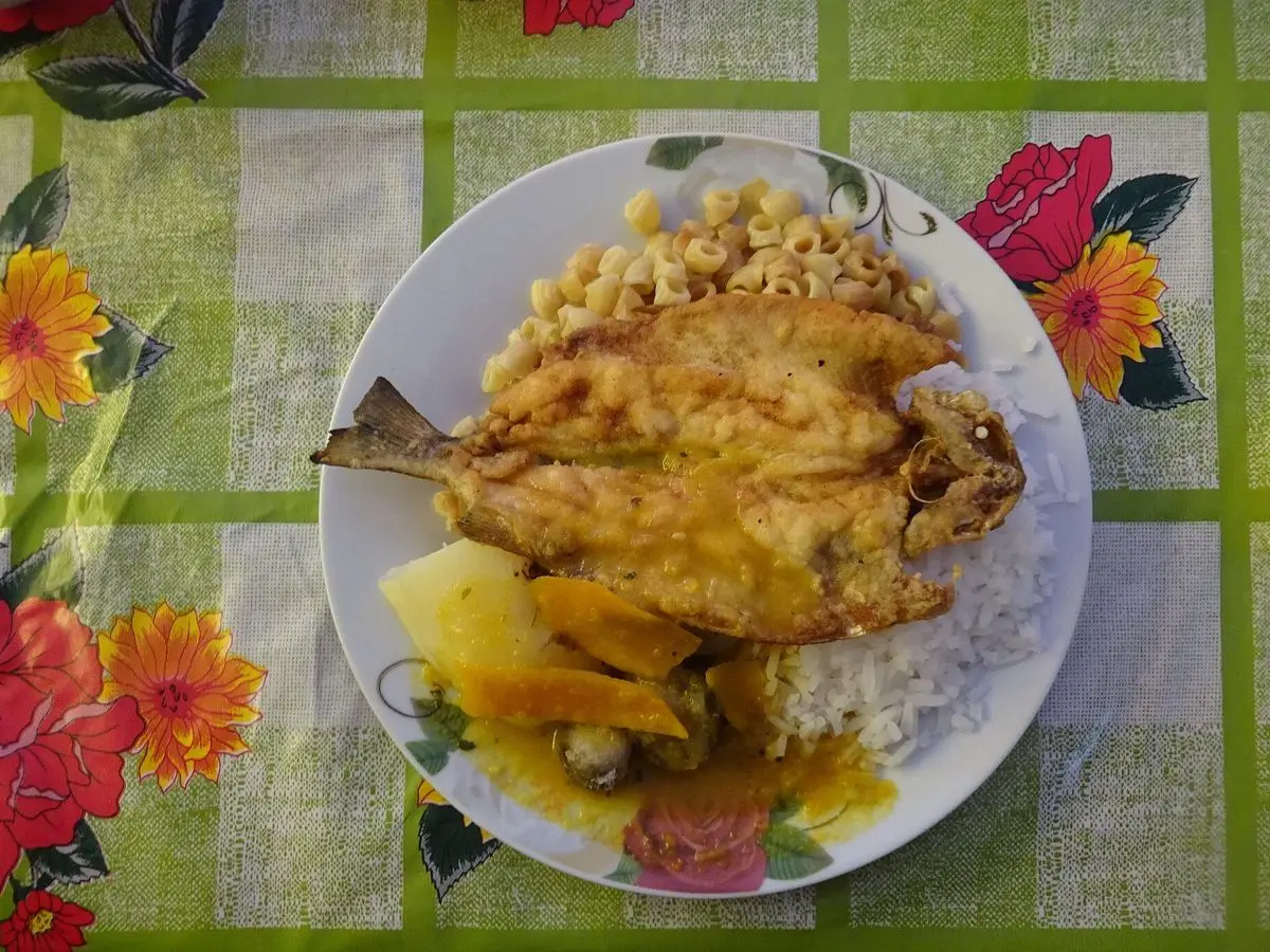Pejerrey frito entero sobre arroz blanco con cebolla y salsa criolla en un plato