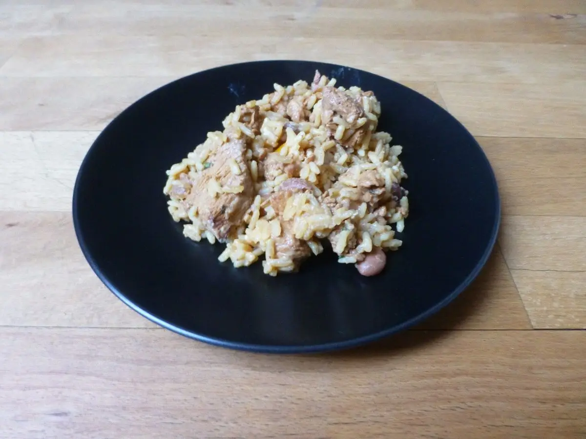 Plato negro con arroz y pollo desmenuzado guisado sobre una mesa de madera