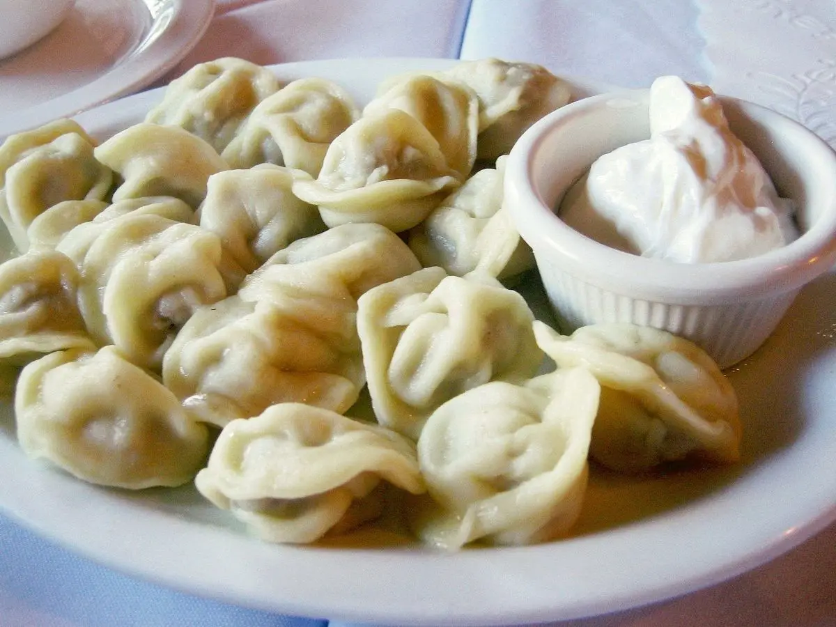 Plato de pelmeni con un cuenco de nata agria al lado