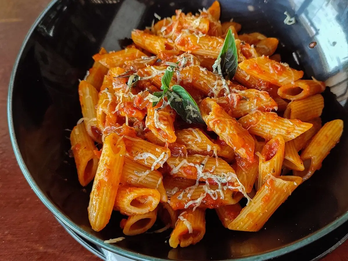 Penne en salsa de tomate picante con albahaca fresca en un plato hondo oscuro