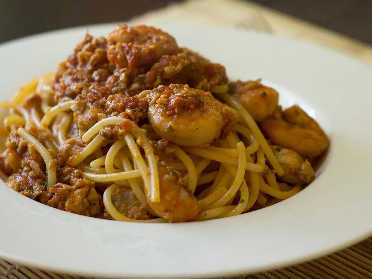 Pasta larga con ragú de pescado y tomate en un plato hondo blanco sobre una mesa de madera