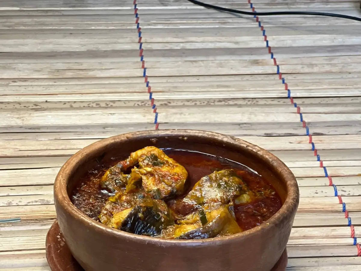 Cuenco de barro con sopa picante de pescado en caldo anaranjado sobre una esterilla de bambú