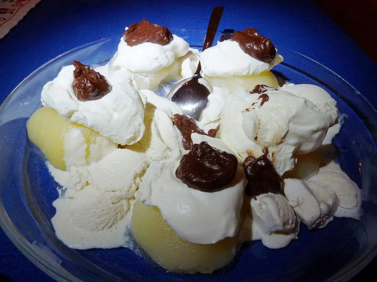 Peras con nata o helado de vainilla y salsa de chocolate en un plato azul
