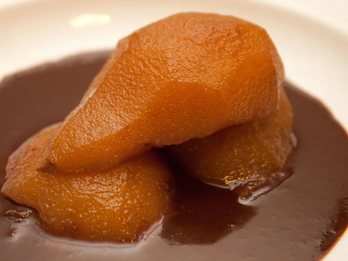 Pera cocida y caramelizada en una salsa oscura servida en un plato hondo blanco